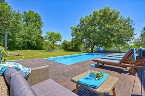 A wooden deck with a pool, lounge chairs, and a table with a blue tablecloth.