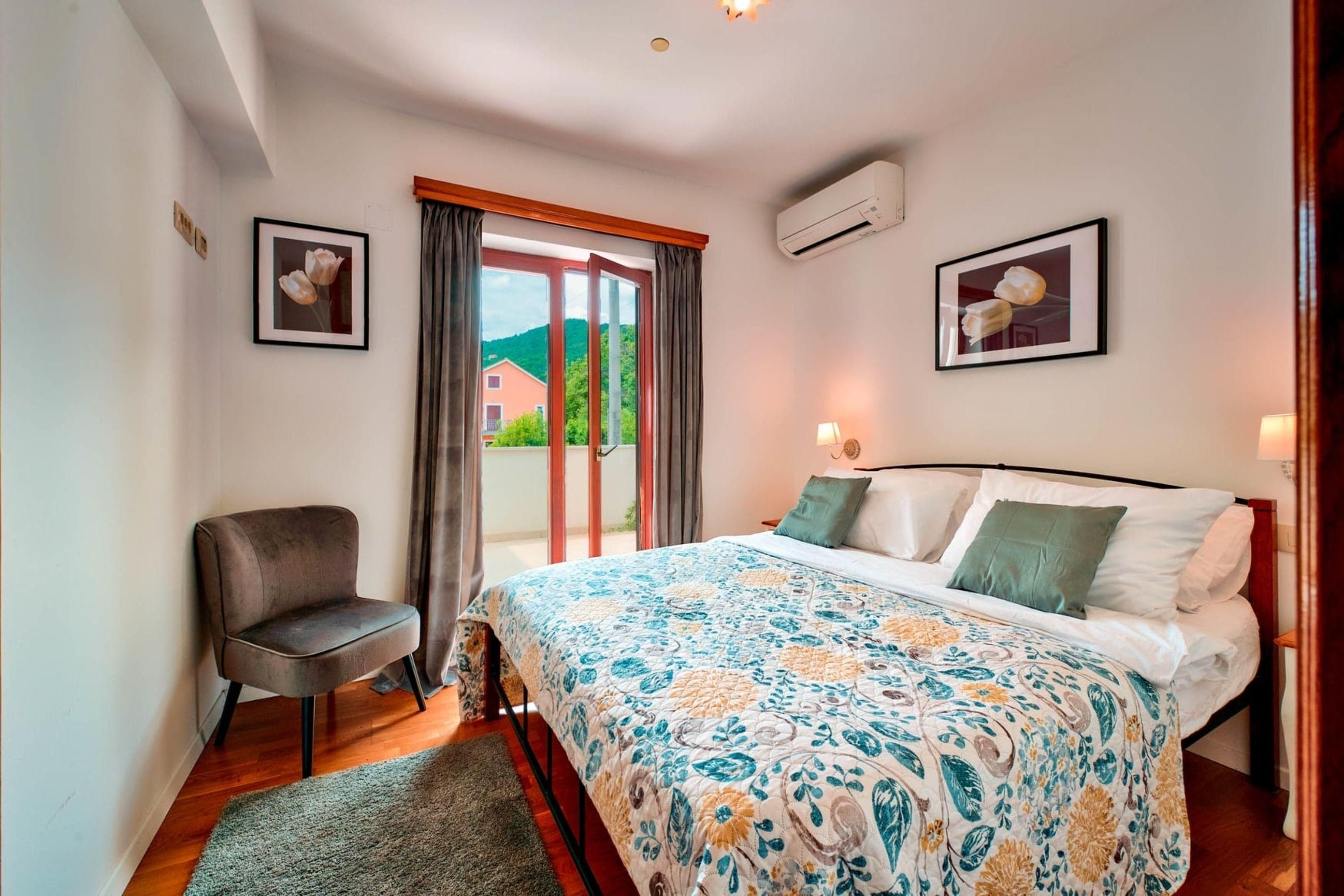 A bedroom with a bed, a chair, a window with curtains, and two framed pictures on the walls.