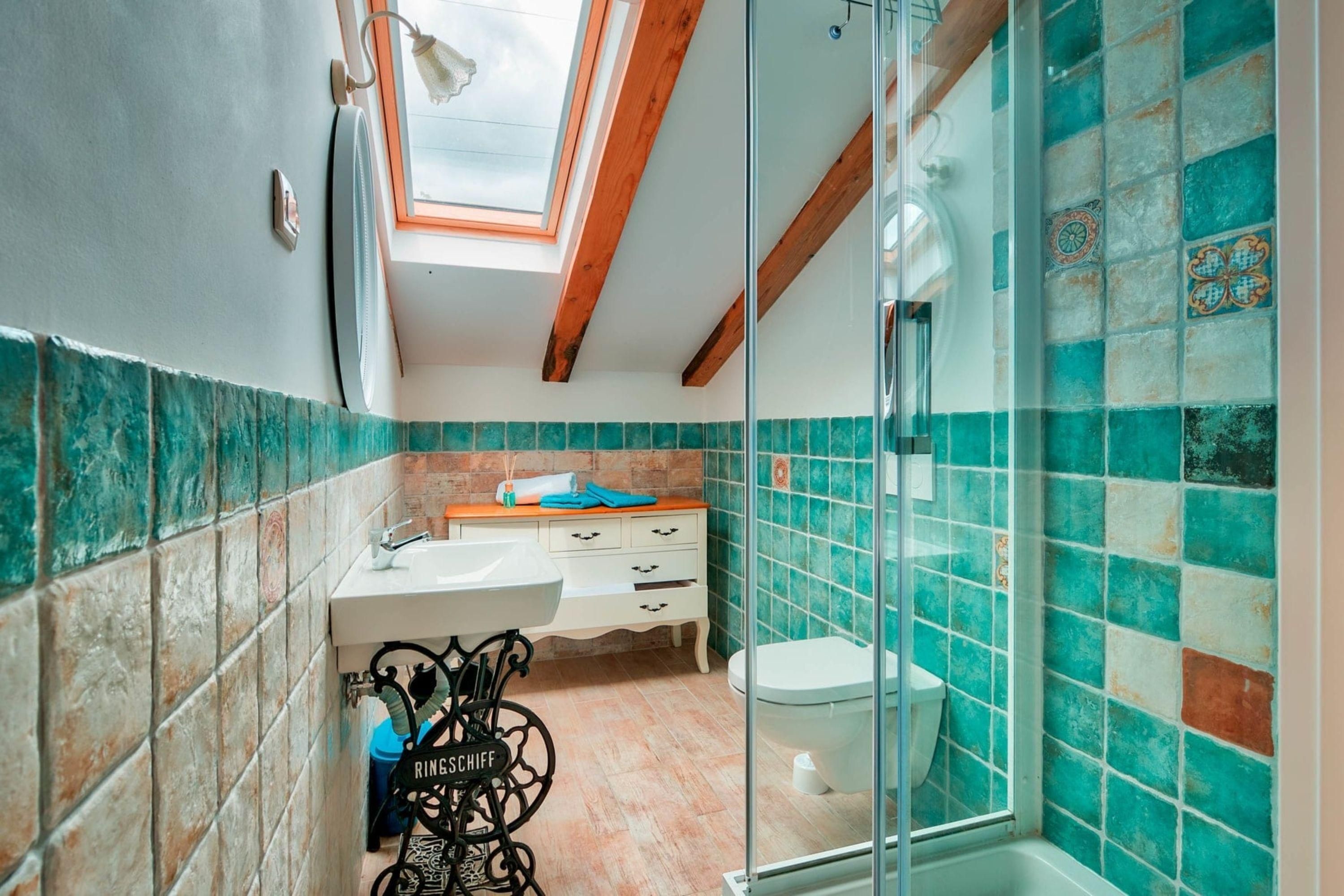A bathroom with a skylight, a sink, a toilet, and a shower area.