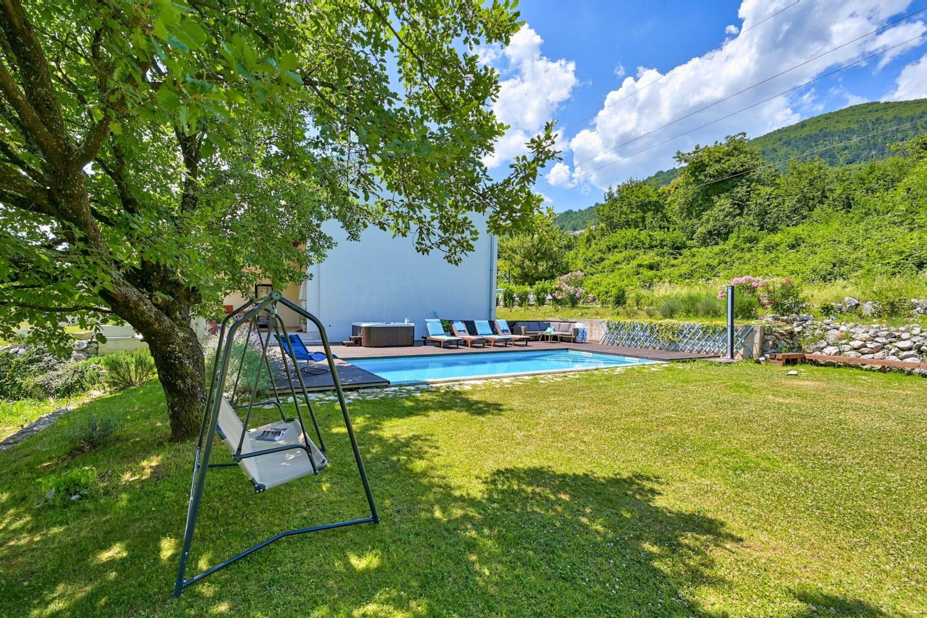 A backyard with a swimming pool, a swing set, and a seating area with lounge chairs.