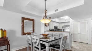 A dining area with a white table and chairs, a chandelier, and a large mirror on the wall.