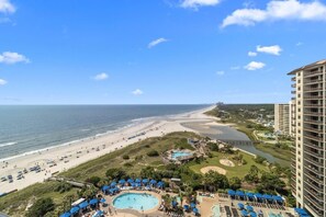 Um resort com piscina grande, acesso à praia e um prédio alto.