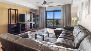 Ein Wohnzimmer mit Ledersofa, einem Glastisch, einem Fernseher und einem Balkon mit Meerblick.