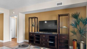 Ein Wohnzimmer mit einem großen Flachbildfernseher, einem dunklen Holz-Entertainment-Center und einem gemusterten Teppich.