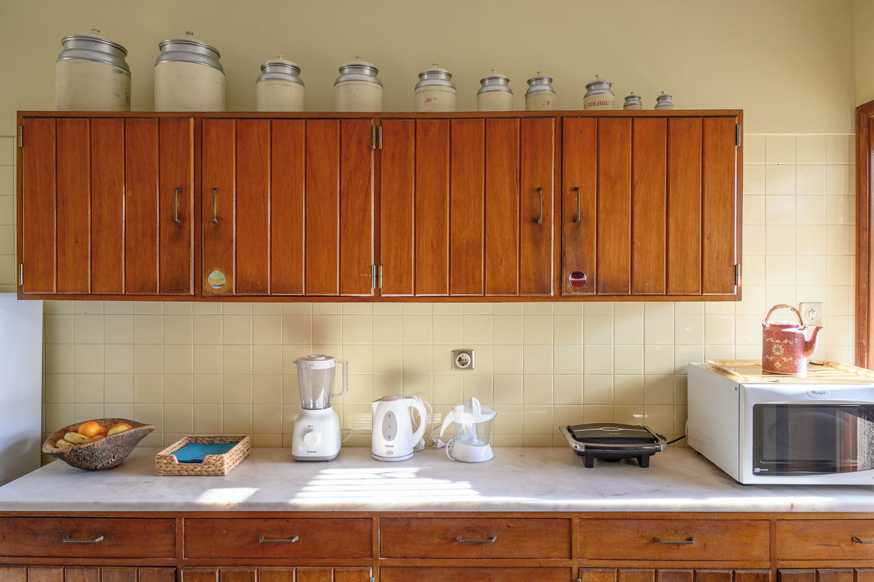 A kitchen with wooden cabinets, a blender, a kettle, a toaster, and a microwave.