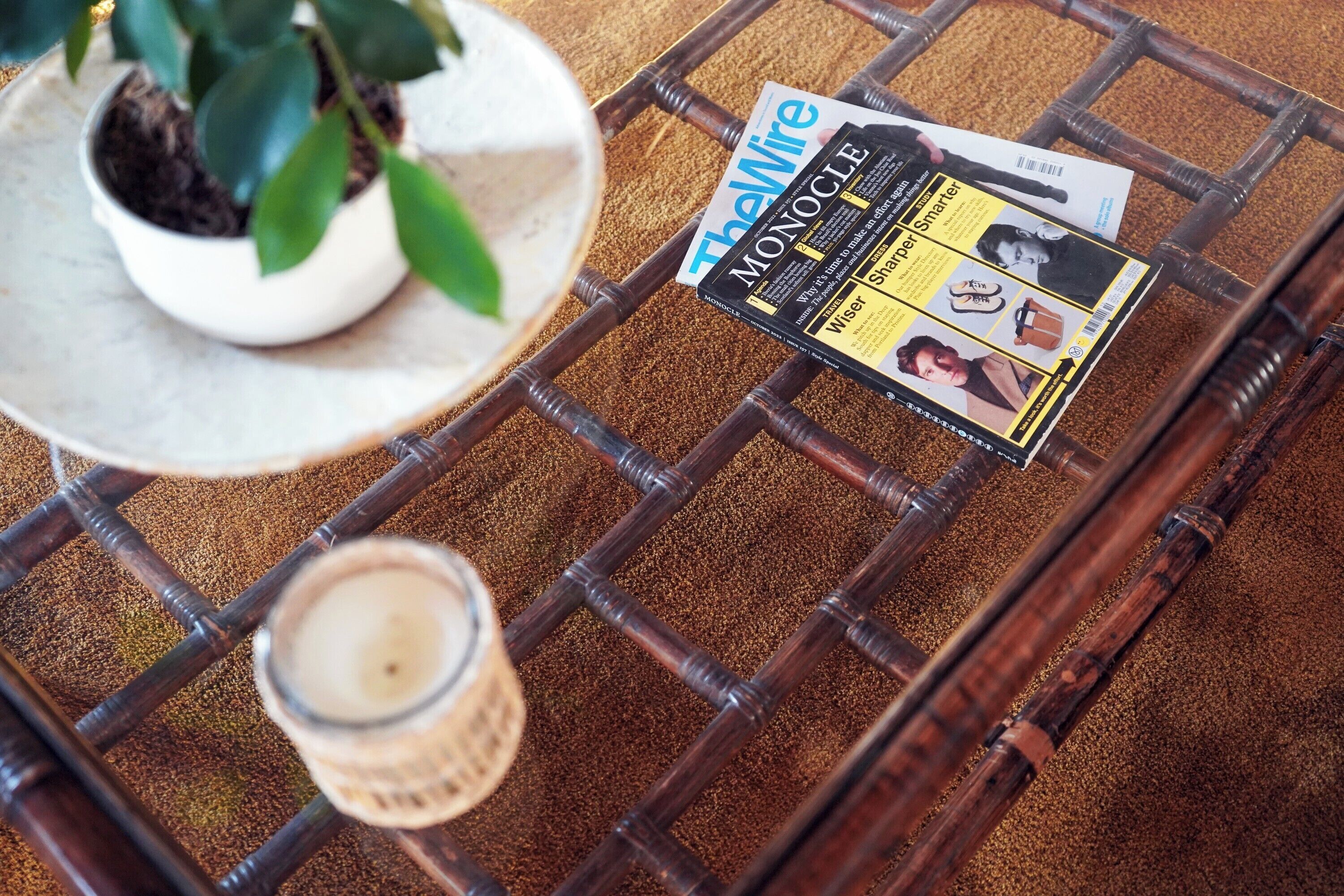 A magazine on a woven table, a potted plant, and a candle.