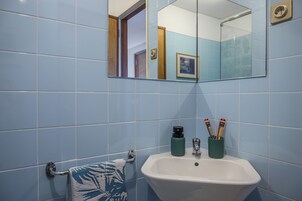A bathroom with blue tiles, a white sink, a towel rack, and a mirror reflecting a door and a framed picture.