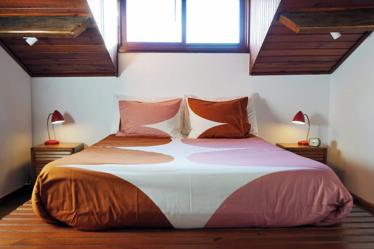 A bedroom with a large bed, wooden headboard, two bedside tables with lamps, and a sloped ceiling.