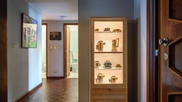 Um corredor com piso de madeira, uma vitrine de vidro com objetos de cerâmica e uma porta com moldura de madeira.