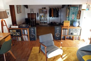 Una sala de estar con piso de madera, un sillón gris, un tapete amarillo y una estantería llena de libros y discos.