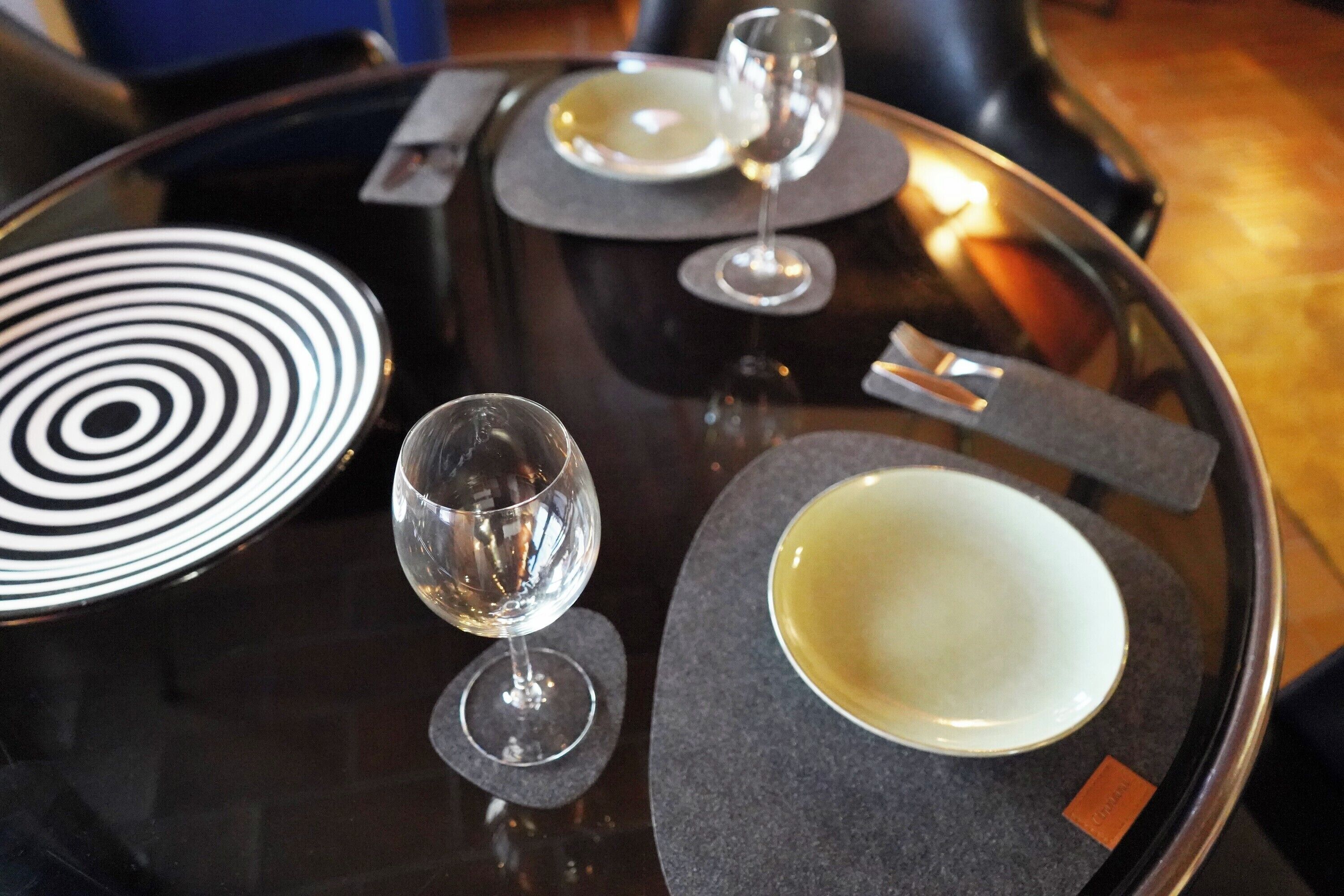 Una mesa redonda con un plato blanco y negro, una copa de vino y un plato blanco con una etiqueta.