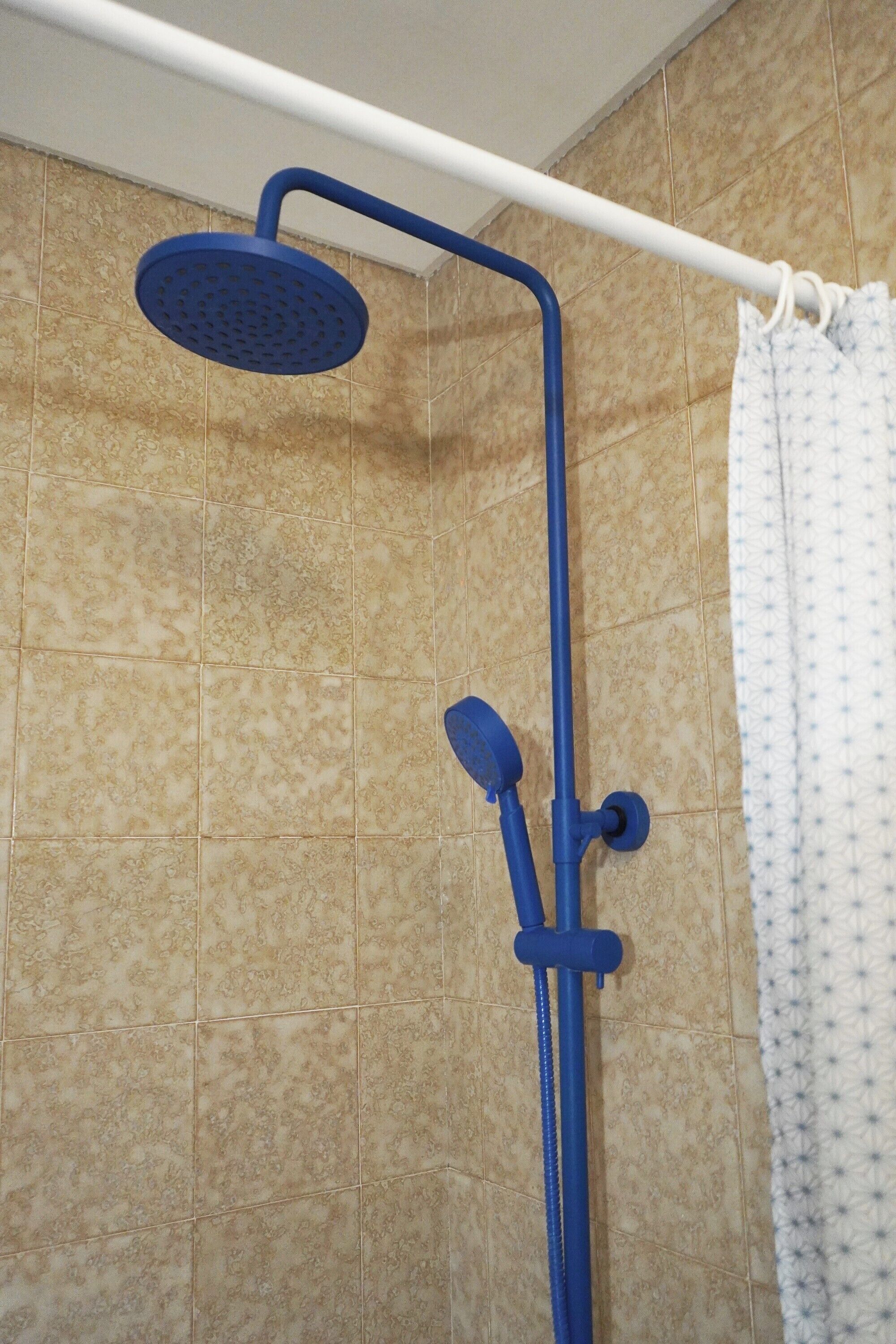 A shower with a blue handheld showerhead and a wall-mounted faucet.