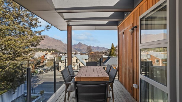 Een balkon met een houten tafel en stoelen, met uitzicht op een bergachtig landschap en een stad.