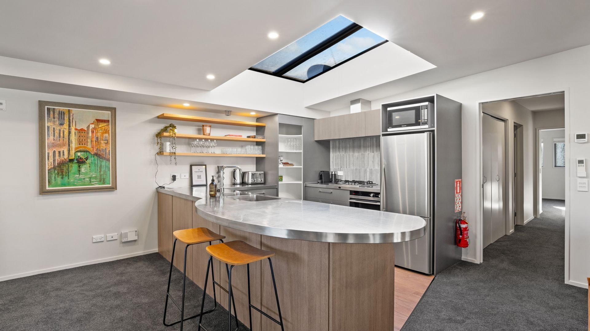 A modern kitchen with a central island, stainless steel appliances, and a skylight.