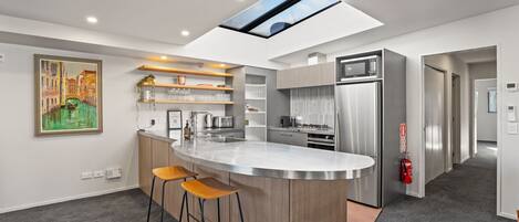 A modern kitchen with a central island, stainless steel appliances, and a skylight.
