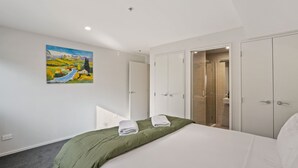 Een slaapkamer met een bed, groen beddengoed, een schilderij aan de muur en een badkamer met een glazen deur.