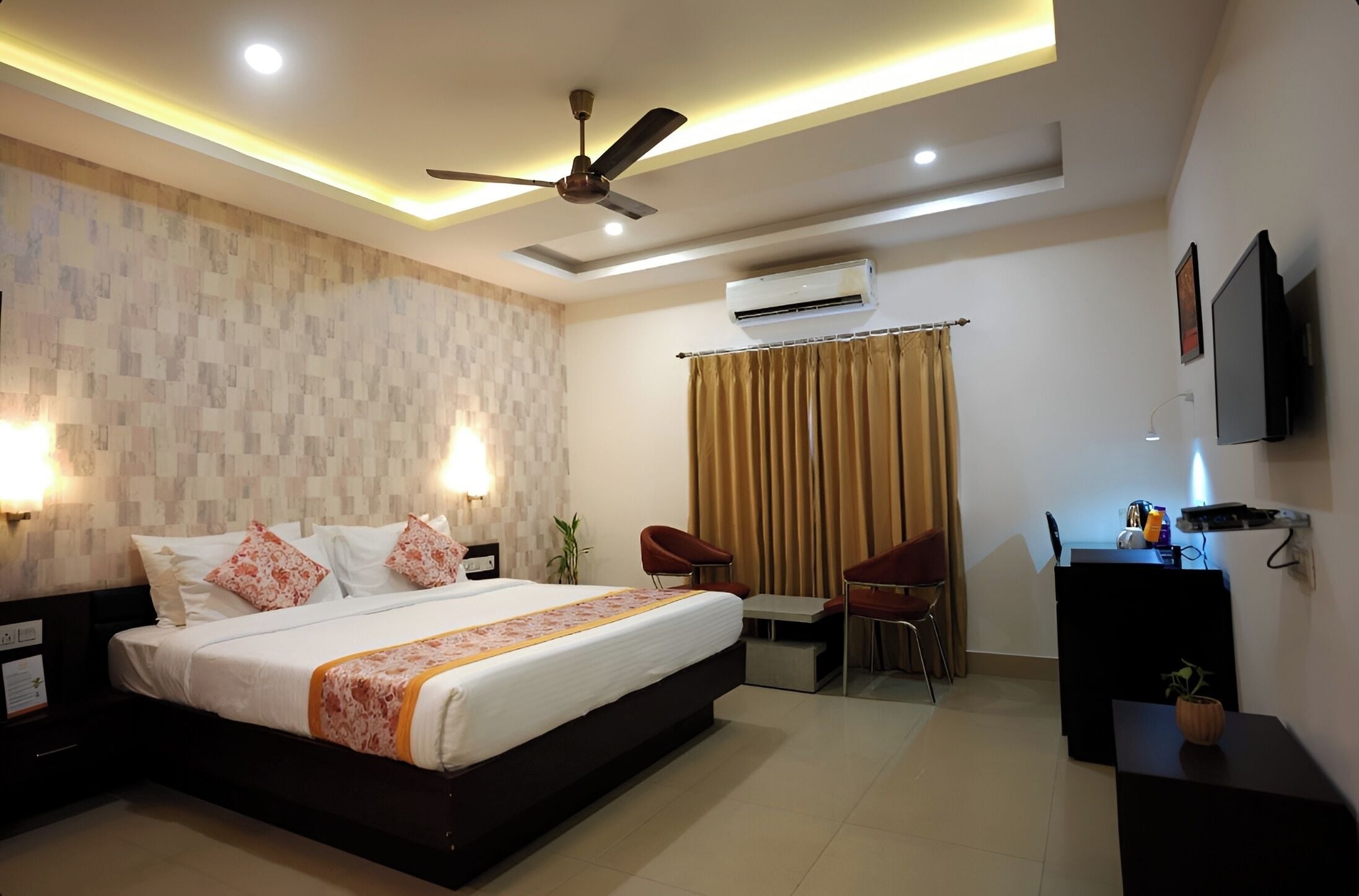Habitación de hotel con cama, mesitas de noche, escritorio, silla, aire acondicionado y ventilador de techo.