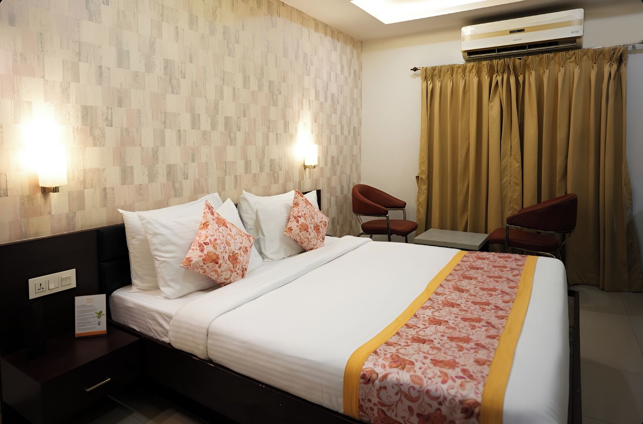 Una habitación de hotel con cama, dos sillas, un escritorio y un equipo de aire acondicionado.