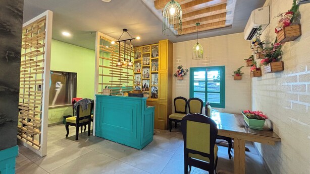 A dining area with a teal-colored counter, wooden chairs, and a table. There are hanging lights and a window with a view. - Sumitel Premier Inn (Siliguri)