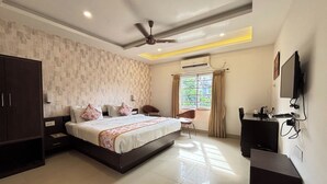 A modern bedroom with a large bed, a wardrobe, a desk with a computer, and a ceiling fan. - Sumitel Premier Inn (Siliguri)