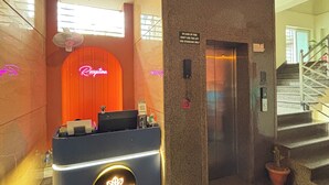A reception desk with a neon sign, a sign instructing to use the stairs in case of fire, and an elevator. - Sumitel Premier Inn (Siliguri)