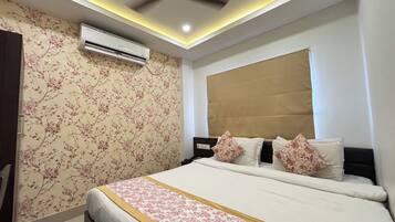 A bedroom with a bed, air conditioning unit, ceiling fan, and floral wallpaper.