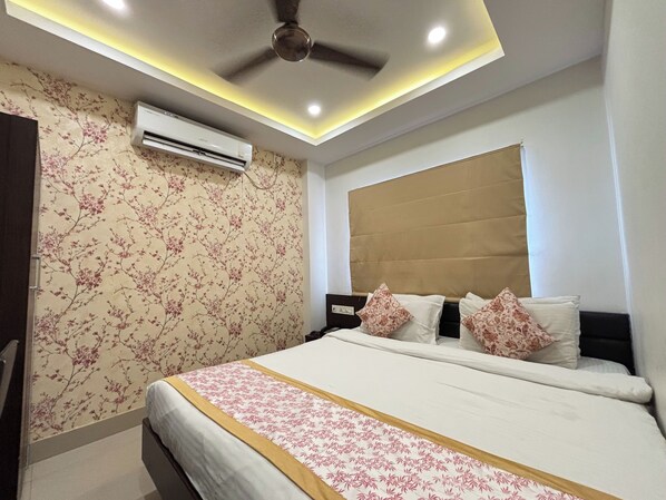A bedroom with a bed, air conditioning unit, ceiling fan, and floral wallpaper. - Sumitel Premier Inn (Siliguri)