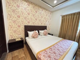 A hotel room with a large bed, a wooden nightstand, a floral wallpaper, and a window with curtains.