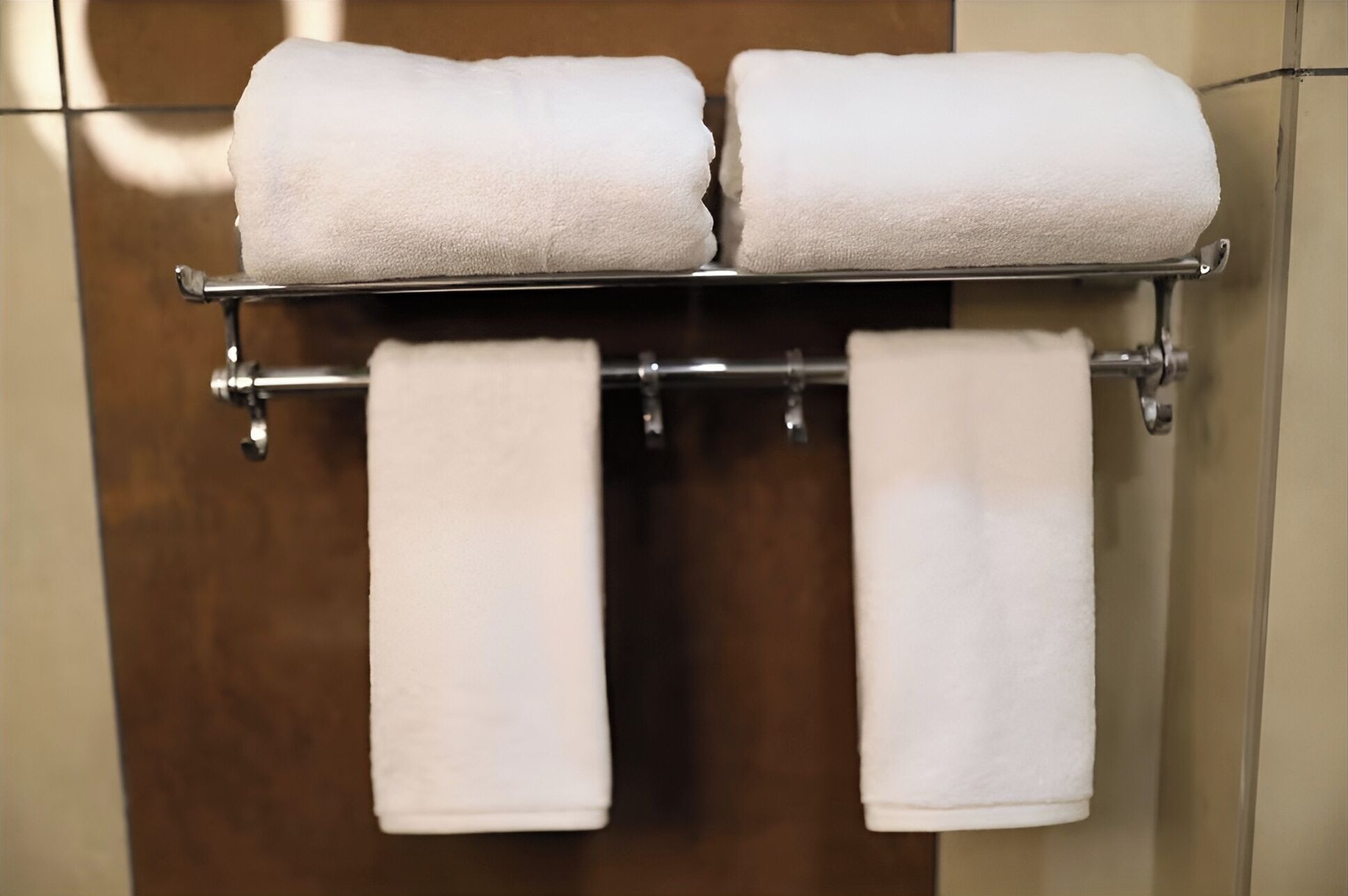Une salle de bain avec un porte-serviettes sur lequel sont posées deux serviettes enroulées et deux autres serviettes suspendues en dessous.