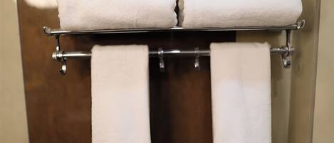 A bathroom with a towel rack holding two rolled towels and two towels hanging below.