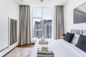 A modern hotel room with a large bed, a view of high-rise buildings, and a window with curtains. - Oceana Baltic Palm West Beach Views 3 Beds (Dubai)