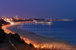 A coastal cityscape at dusk with illuminated buildings and a long pier extending into the water. - Cosy Bee  (Bournemouth)