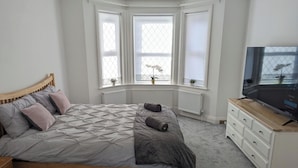 A bedroom with a bed, a TV, a dresser, and a bay window. - Cosy Bee  (Bournemouth)