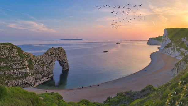 A coastal landscape with a natural rock arch, a sandy beach, and cliffs. - Cosy Bee  (Bournemouth)