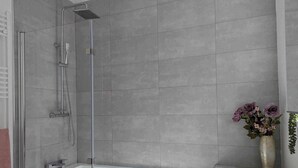 A modern bathroom with a glass-enclosed shower, a white bathtub, and a vase with flowers on the countertop. - Cosy Bee  (Bournemouth)