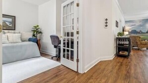 A room with a white wall, a wooden floor, a bed, a desk, and a chair. - Birdies & Beaches Getaway, Golf and Beach Retreat (Pender County)