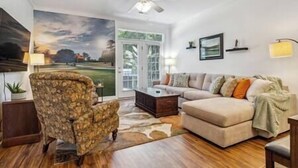 A living room with a stone accent wall, a sofa, a coffee table, and a ceiling fan. - Birdies & Beaches Getaway, Golf and Beach Retreat (Pender County)