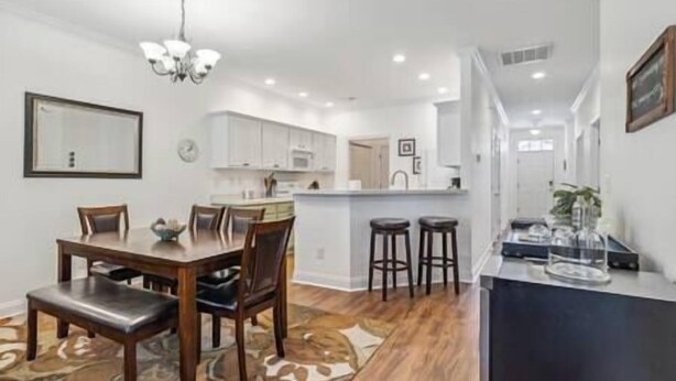 A modern kitchen with white cabinets, a central island, and a dining area with a wooden table and chairs. - Birdies & Beaches Getaway, Golf and Beach Retreat (Pender County)