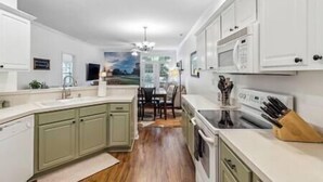 A modern kitchen with white cabinets, a central island, and a dining area with a view. - Birdies & Beaches Getaway, Golf and Beach Retreat (Pender County)