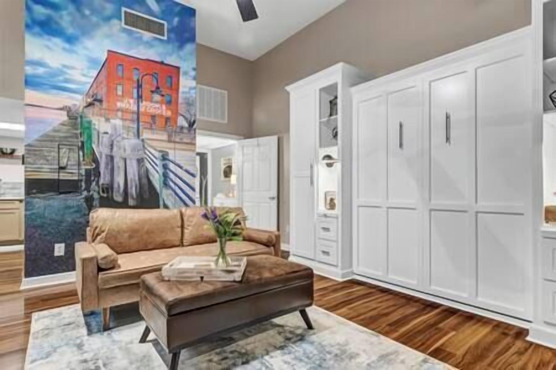 A modern living room with a brown leather sofa, a coffee table, and a painting of a building on the wall.