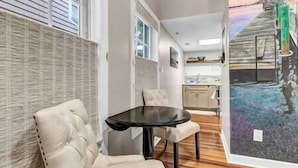 A room with a dining table and chairs, a kitchen in the background, and a large painting on the wall. - Water Street Hideaway (Wilmington)
