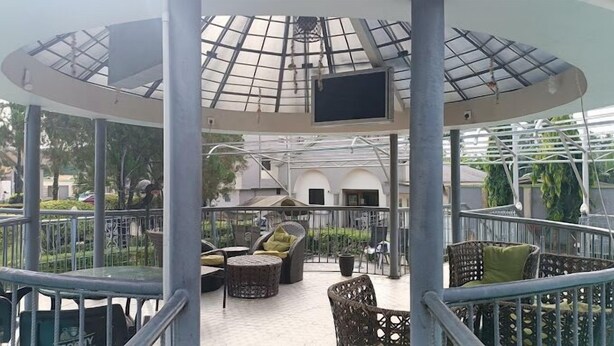 A covered outdoor area with a glass ceiling, seating arrangements, and a television screen. - Lushville Hotel and Suites  (Benin City)