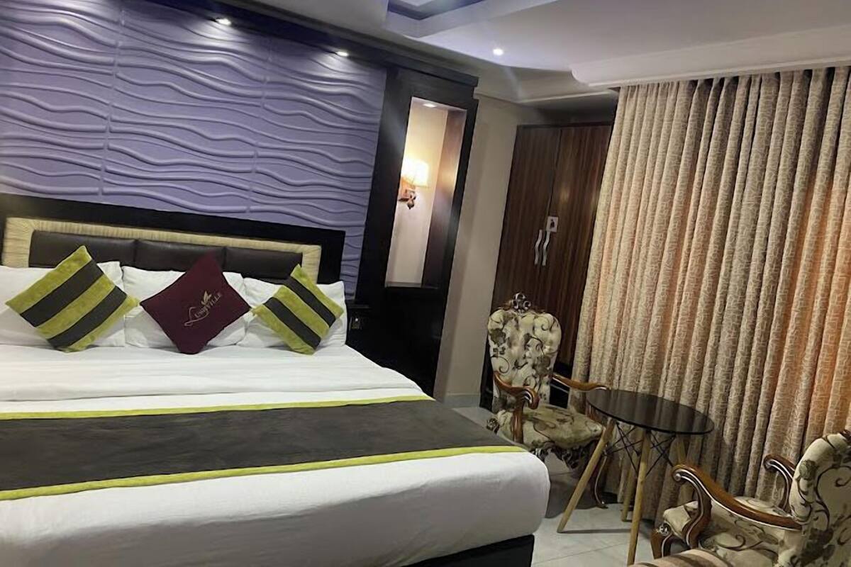 Una habitación de hotel con una cama grande, un armario de madera, una mesita redonda y una silla.