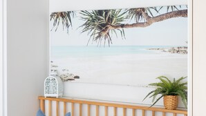 Une chambre à coucher avec une décoration murale sur le thème de la plage, un climatiseur blanc, une tête de lit en bois et deux coussins bleus.