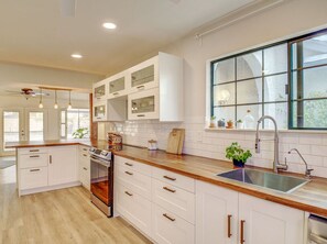 A modern kitchen with white cabinetry, wooden countertops, a built-in oven, and a large window with a view. - Royale Living in the Heart of Phoenix (Glendale)