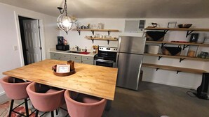 Eine kompakte Küche mit einer Holzeile, rosa Stühlen, einem Edelstahlkühlschrank und Einbaukästen.