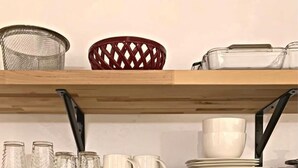 Eine Küche mit Holzböden, die Glaskolben, weiße Tassen und Teller beherbergen. Darunter befindet sich ein Behälter mit Holzkochtöpfen und einem Frigidaire-Ofen.