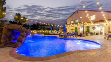A swimming pool with a rock feature and lounge chairs, surrounded by a patio area with string lights.