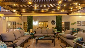 Ein gemütlicher Außenbereich mit Sofas und Tischen, einer Pergola mit Lichterketten und einem an der Wand befestigten Schild.