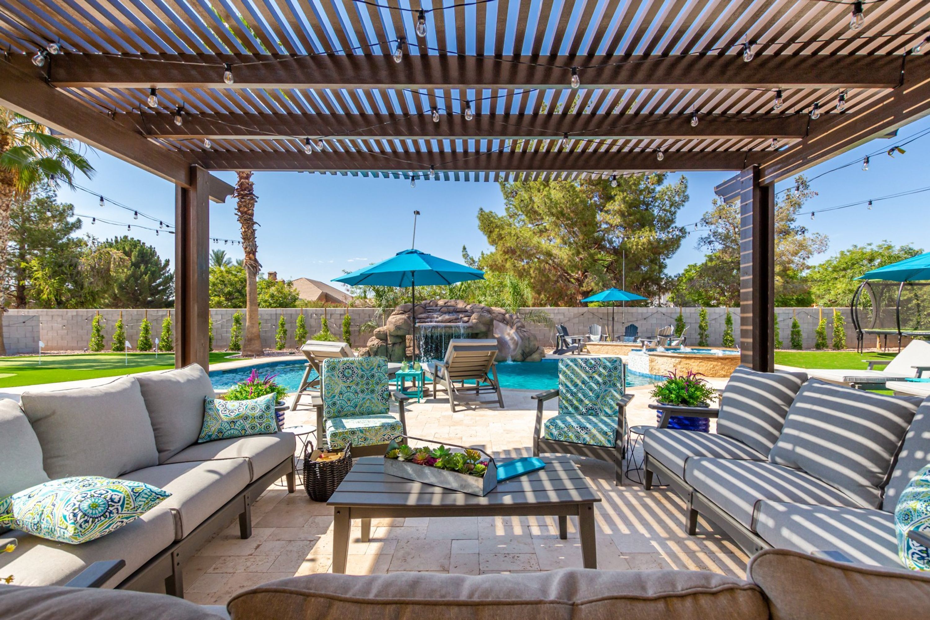Ein Außenbereich mit Terrasse, Pool, Sitzgelegenheiten und einer Pergola mit Lichterketten.